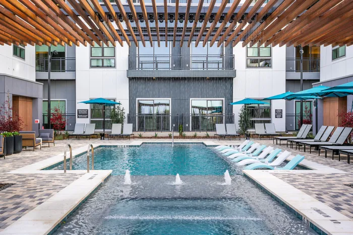 Luxurious apartment community with a sparkling pool, elegant sun loungers, and stylish pergolas, perfect for relaxation and leisure.