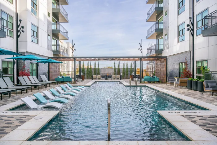 Modern luxury apartment complex with a sparkling outdoor pool, stylish sun loungers, vibrant umbrellas, and cozy seating areas for relaxation.