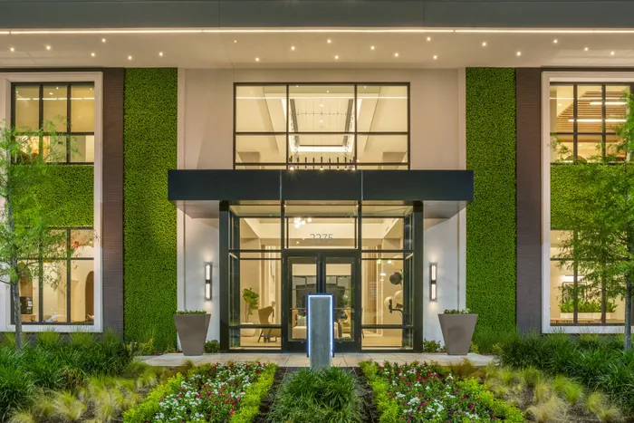 Modern apartment building entrance with elegant glass doors, vibrant green walls, and inviting landscaping.