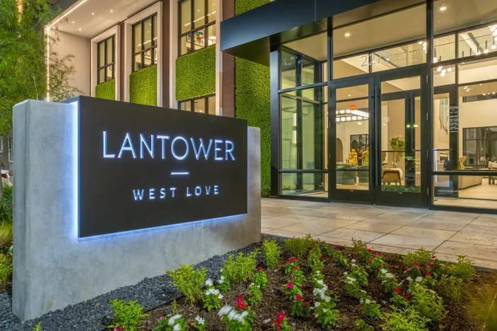 Luxurious entrance of Lantower West Love with illuminated sign, lush greenery, and stylish glass doors.