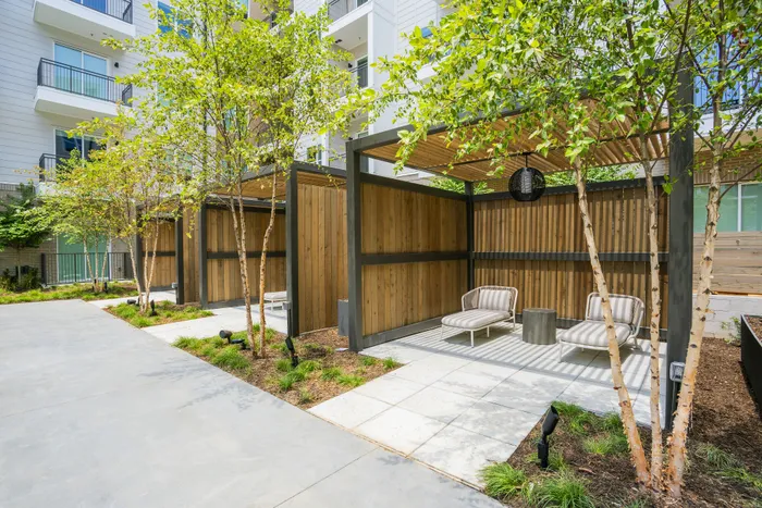 Modern outdoor patio area with stylish wooden pergolas, lush greenery, and comfortable lounge chairs, perfect for relaxation and entertaining.