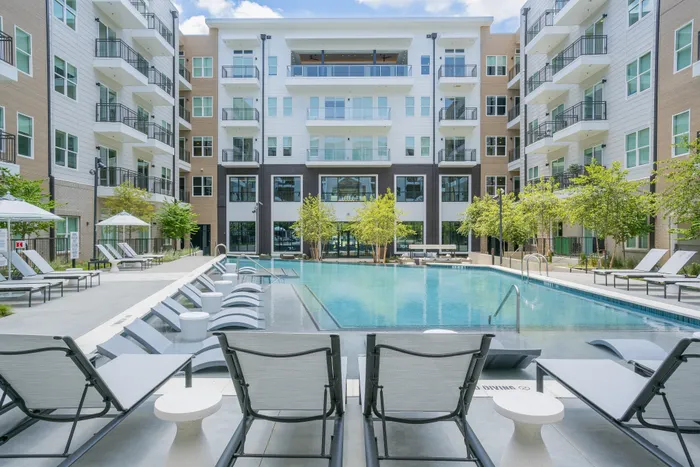Luxurious apartment complex featuring a stunning outdoor pool area with modern lounge chairs and green landscaping.