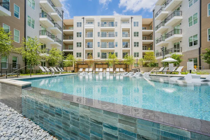Luxurious apartment complex featuring a sparkling swimming pool surrounded by stylish loungers and elegant landscaping.