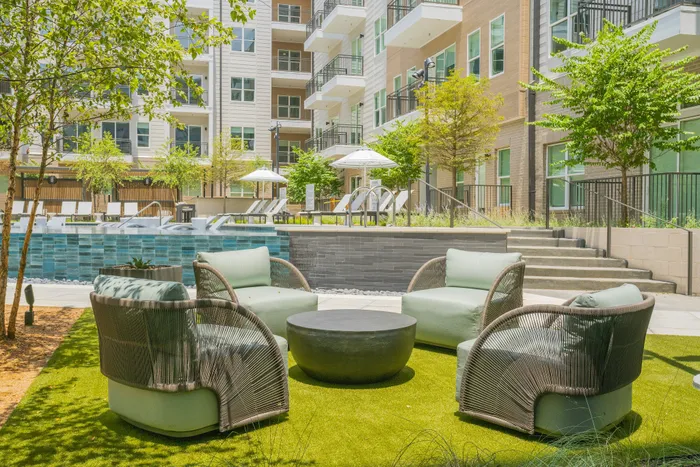 Modern apartment courtyard featuring stylish outdoor seating, lush greenery, and an inviting pool area.