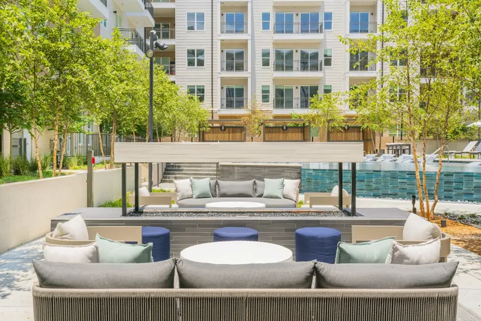 Modern apartment courtyard featuring stylish outdoor seating, lush greenery, and a refreshing swimming pool against a backdrop of elegant multi-story buildings.