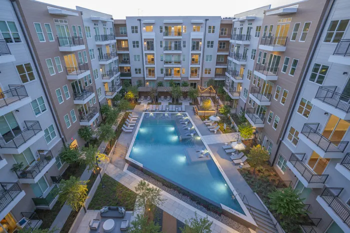 Chic apartment complex featuring a luxurious rooftop pool surrounded by lounge chairs and lush greenery, perfect for relaxation and social gatherings.