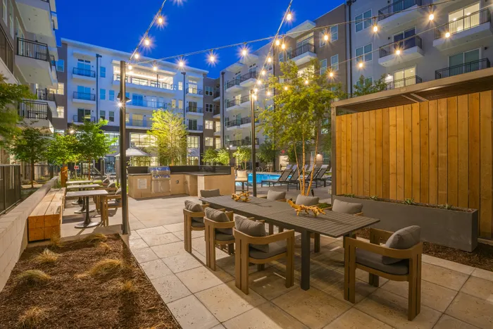 Elegant apartment courtyard at night featuring stylish outdoor seating, string lights, modern architecture, and a sparkling pool.