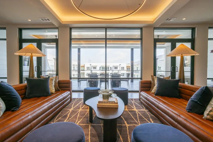 Elegant living room with luxurious brown leather sofas, modern lighting, and expansive windows offering a scenic view.