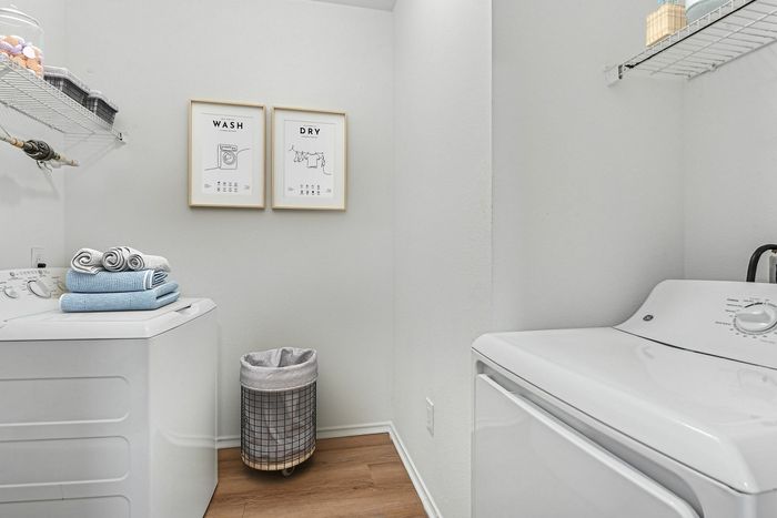 Chic and efficient laundry room featuring modern appliances, stylish artwork, and neatly organized storage.