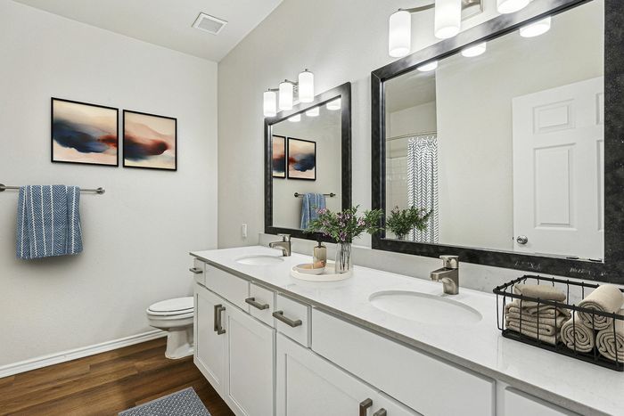 Elegant bathroom featuring dual sinks with sleek fixtures, modern artwork, and stylish lighting, complemented by plush towels and decorative plants.