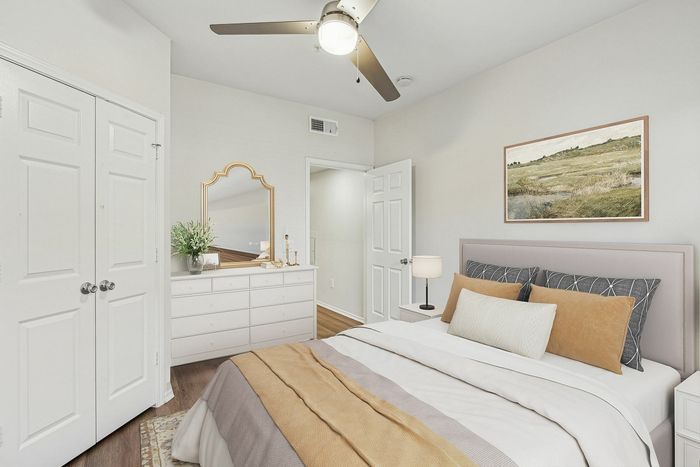 Inviting bedroom with elegant decor, featuring a cozy bed with stylish cushions, warm lighting, framed artwork, and a chic mirrored dresser.