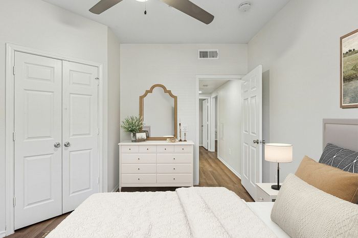 Bright and inviting bedroom featuring a cozy bed with textured bedding, elegant dresser with mirror, and stylish decor accents, all set on warm wooden flooring.