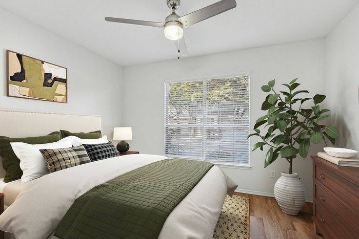 Inviting bedroom with a modern ceiling fan, sunlit window, lush indoor plant, and stylish bedding featuring green accents.