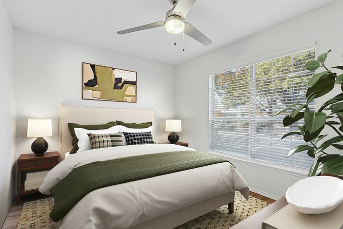 Bright and cozy bedroom with modern decor, featuring a stylish bed with green accents, a ceiling fan, and large windows that allow ample natural light.