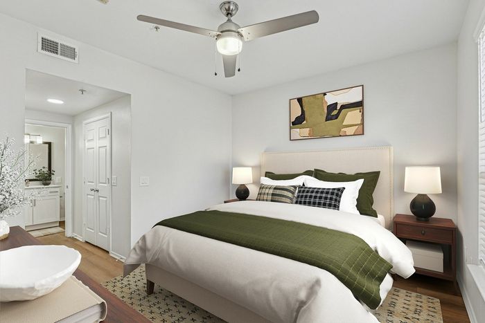 Elegant bedroom with a plush bed adorned in green and white, stylish ceiling fan, and contemporary art accent. Features a cozy atmosphere with natural light and a modern ensuite bathroom.