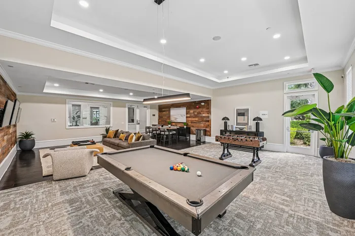 Luxurious recreational room featuring a stylish pool table, comfortable seating area, foosball table, and modern decor with lush greenery.