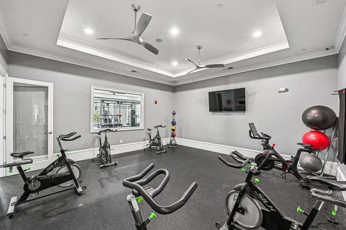 Modern fitness room equipped with sleek exercise bikes, ceiling fans, and vibrant stability balls, offering a bright and inviting workout space.
