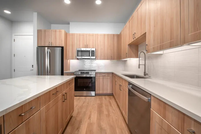 Modern kitchen with sleek wooden cabinetry, stainless steel appliances, and elegant white countertops, perfect for gourmet cooking.