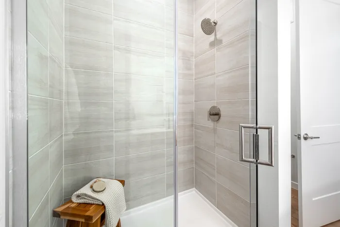 Elegant bathroom shower with modern grey tiles, glass door, and wooden stool for a luxury spa-like experience.