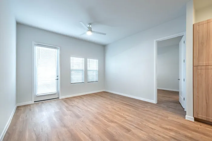 Bright, spacious room with elegant wood flooring, large windows, and modern ceiling fan, offering a serene and welcoming living area.