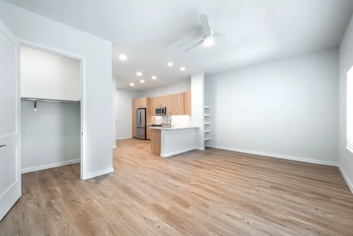 Bright and modern open-concept apartment with stylish wooden flooring, sleek kitchen featuring stainless steel appliances, and built-in shelves for elegant storage solutions.