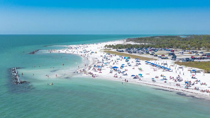 Breathtaking aerial view of a pristine beach with sunbathers, vibrant umbrellas, and turquoise waters, showcasing a perfect coastal escape.