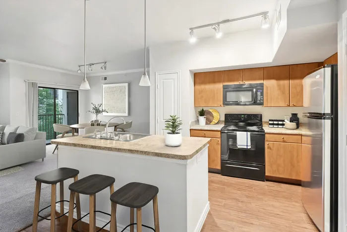 Modern open-concept kitchen and living area with stylish bar seating, warm wood cabinetry, and elegant lighting, leading to a cozy dining space with balcony access.