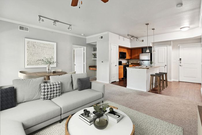 Modern apartment living area featuring a cozy gray sofa, elegant dining setup, and a sleek open kitchen with wood cabinets and bar seating.