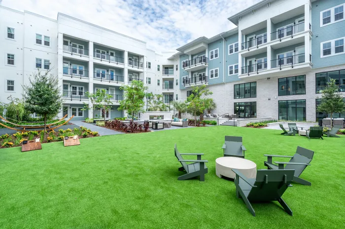 Luxury apartment complex exterior featuring modern architecture, lush green lawn, and outdoor seating area with cozy hammocks and recreational space.