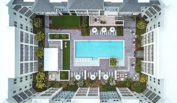 Aerial view of a luxurious apartment complex featuring a sparkling swimming pool, stylish lounge areas, and lush landscaping.