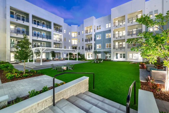 Luxurious apartment complex with modern architecture, featuring a vibrant green courtyard and elegant outdoor seating areas.