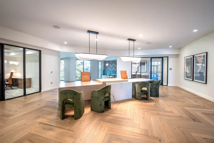 Elegant co-working space with modern lighting, stylish green chairs, and chic herringbone wood flooring.