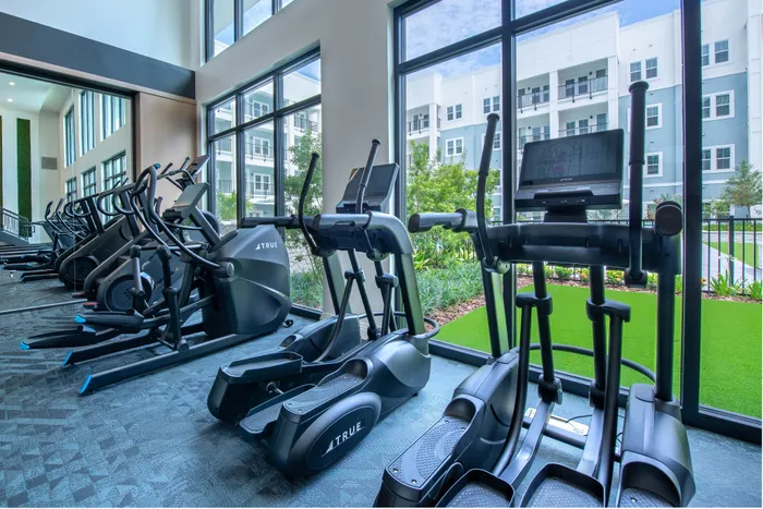 Modern fitness center with state-of-the-art cardio machines and vibrant views of lush greenery, offering a perfect workout ambiance.