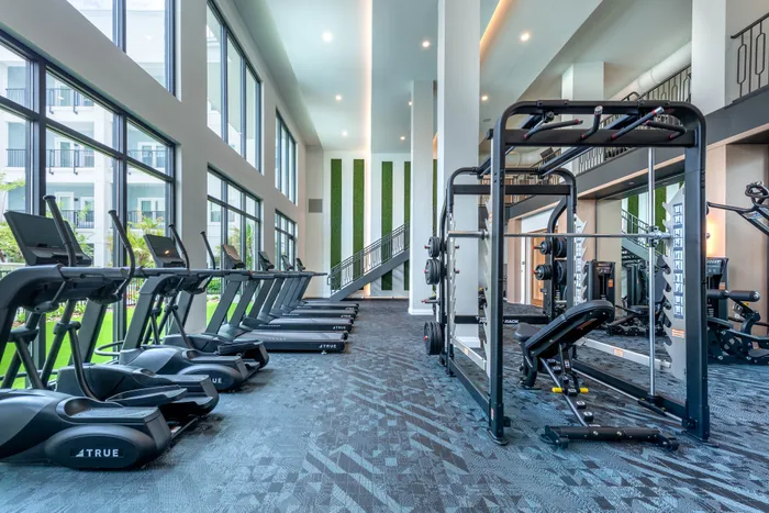 Luxurious fitness center featuring state-of-the-art treadmills, strength training equipment, and expansive windows with a garden view.