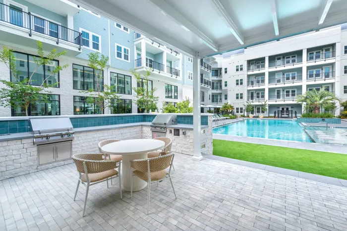 Luxurious outdoor patio area with modern grill and seating overlooking a sparkling pool in a stylish apartment complex.