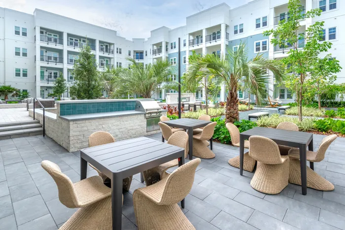 Elegant outdoor courtyard with chic seating, lush greenery, and modern grill, set against a backdrop of stylish apartment balconies.