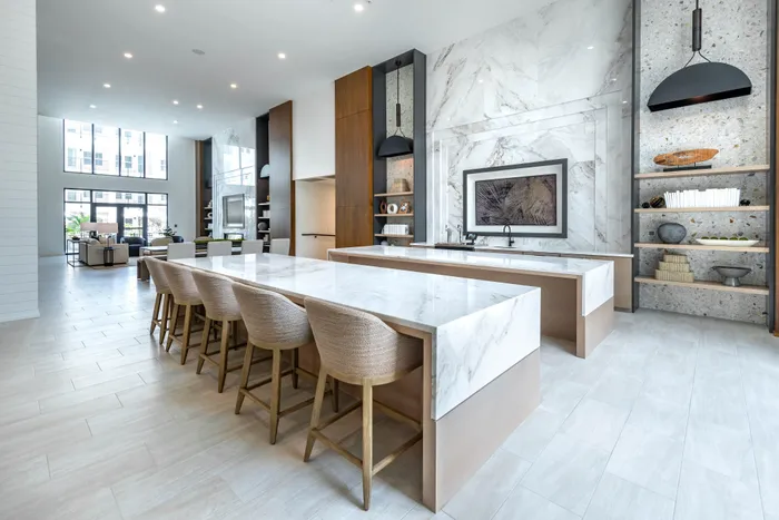 Contemporary open-concept kitchen and dining area with elegant marble countertops, chic barstools, and floor-to-ceiling windows providing ample natural light.