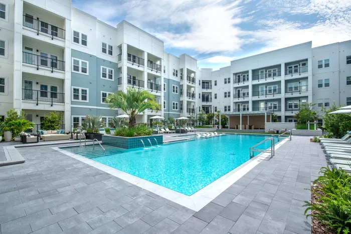 Modern apartment complex with pristine swimming pool, lush greenery, and inviting lounging areas.
