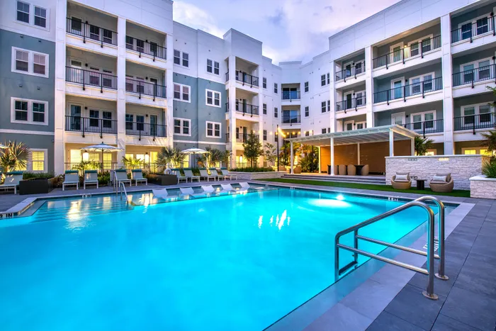 Luxurious apartment complex with a stunning illuminated pool, modern outdoor lounge area, and stylish balconies.