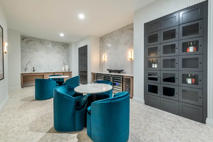 Elegant modern lounge area featuring plush teal chairs, marble tables, and a stylish wine cabinet for a luxurious touch.