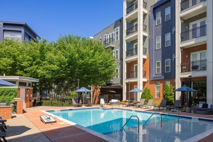 Luxurious apartment complex featuring a pristine outdoor pool with modern lounge areas and stylish building facades.