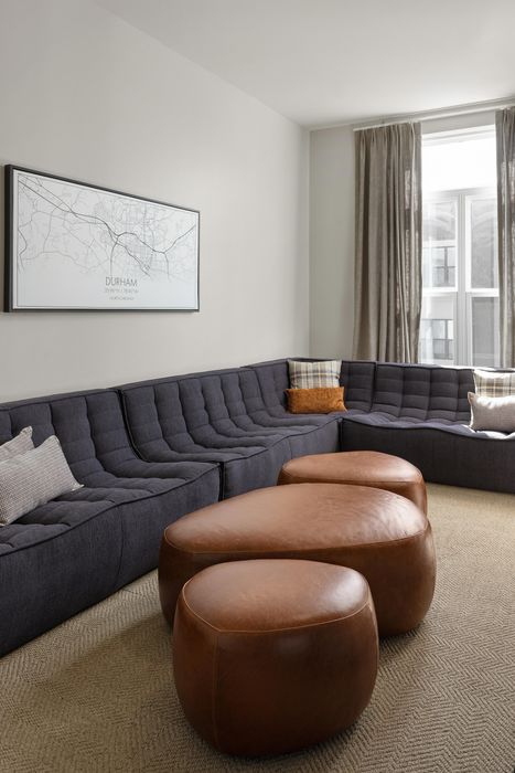 Chic living room with a stylish gray sectional sofa, elegant wall art, and cozy leather poufs, creating a comfortable and modern atmosphere.