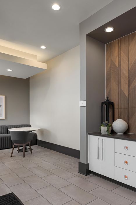 Modern apartment interior showcasing a stylish seating area with a sleek round table, chic gray chair, and built-in cabinetry against elegant wood paneling.