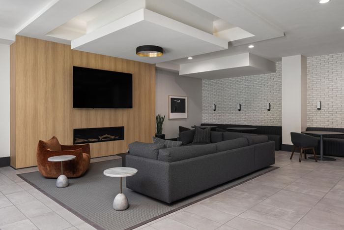 Modern living room with stylish gray sofas, a cozy armchair, sleek wooden accent wall, mounted TV, and ambient lighting.