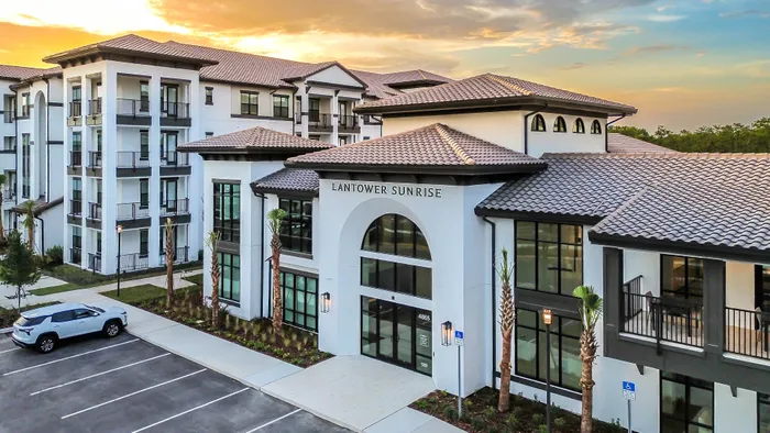 Modern apartment complex with elegant architecture and lush landscaping under a vibrant sunset sky.