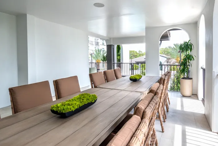 Elegant open-air dining area with spacious wooden table, comfortable wicker chairs, and lush greenery, offering a serene view and modern design.