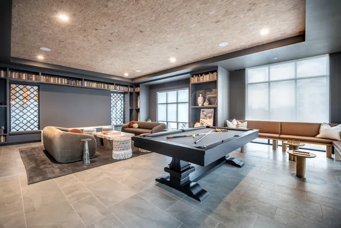 Luxurious lounge area featuring a sleek pool table, cozy seating, and elegant shelving with books in a bright, modern apartment.