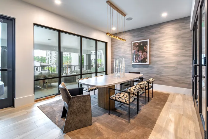 Elegant dining room with a modern table, chic chairs, and stunning floor-to-ceiling windows offering a beautiful balcony view.
