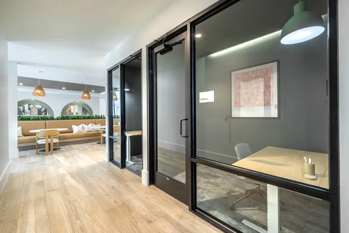 Contemporary office space with sleek glass doors, natural wood flooring, and stylish lounge area.