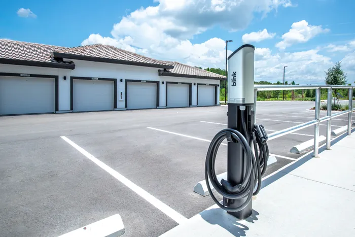 Modern apartment complex with stylish garages and convenient electric vehicle charging station, under a bright blue sky.